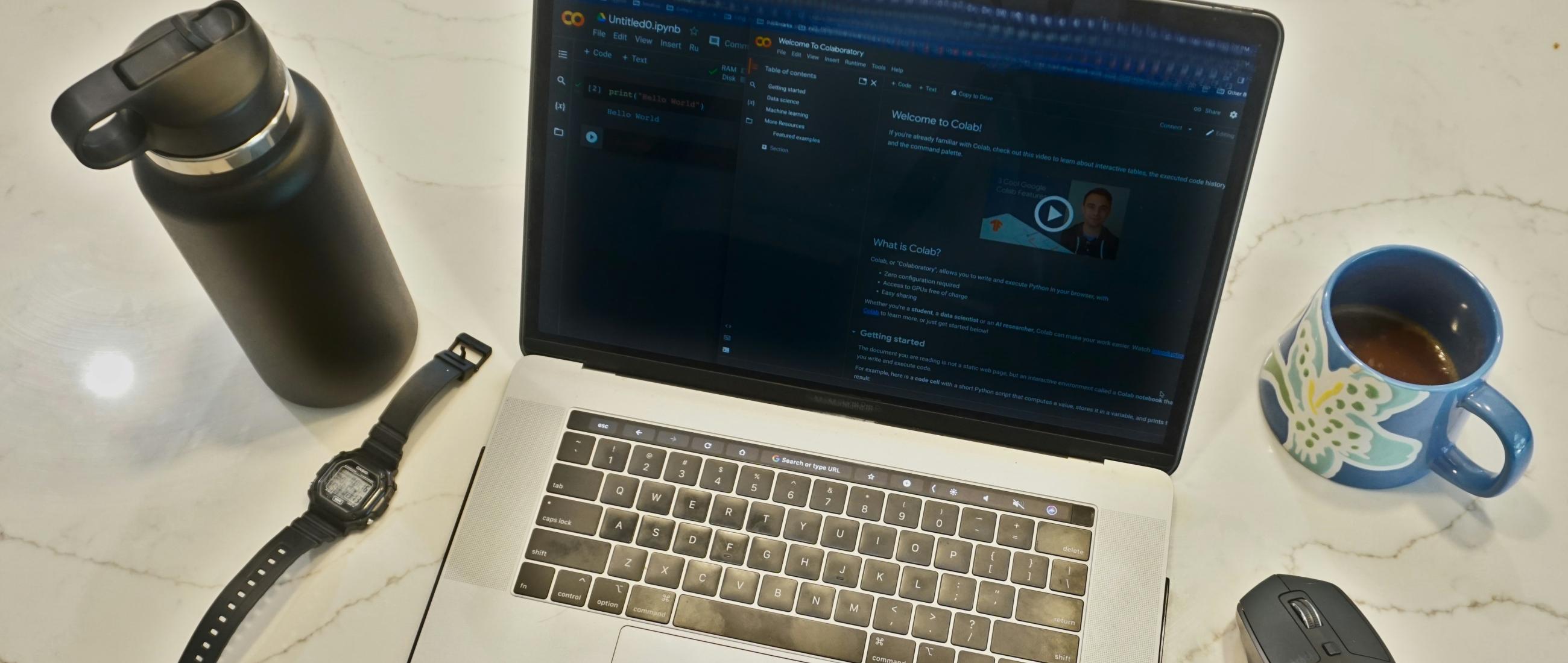 A laptop on a desk with utilities like coffee mug, watch, mouse surrounding it