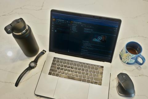 A laptop on a desk with utilities like coffee mug, watch, mouse surrounding it