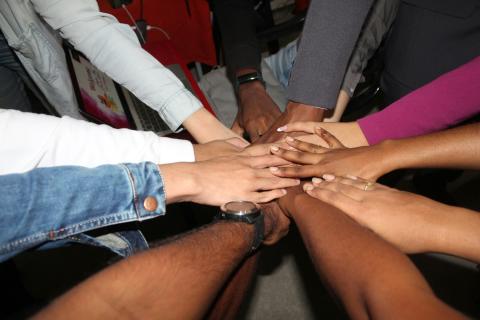 Many hands joined together over a table, representing the Drupal community coming together during the Association's leadership transition